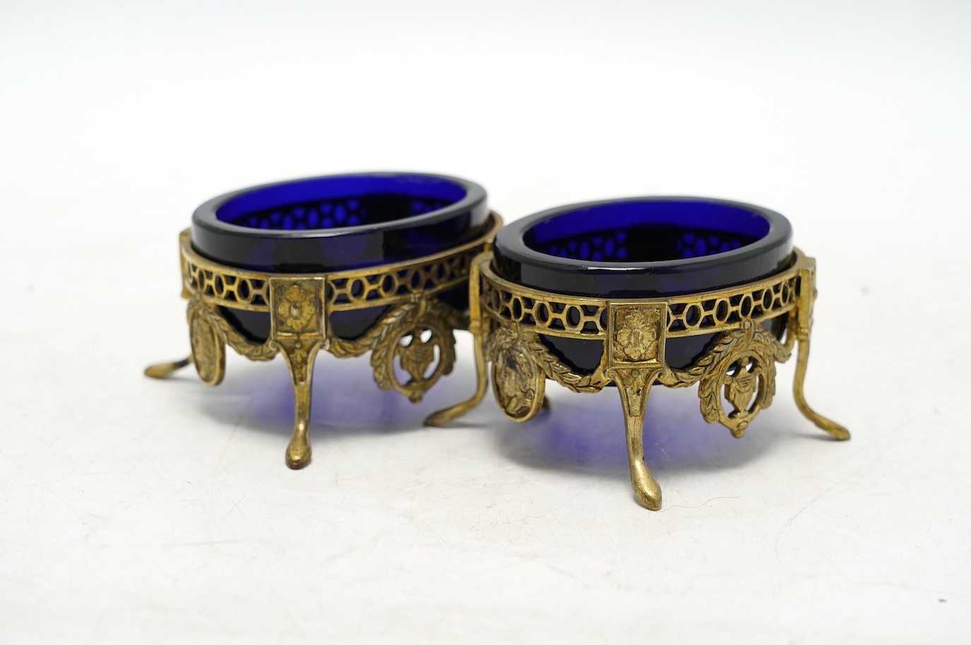 A pair of late 19th/early 20th century continental pierced gilt white metal oval salts, with blue glass liners, 69mm. Condition - fair